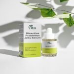 Eine 30-ml-Flasche und eine Verpackung des Vita Elixia Bioactive Prebiotics Jelly Serum zur Stärkung der Hautbarriere, ausgestellt im Schatten eines zarten botanischen Blattes